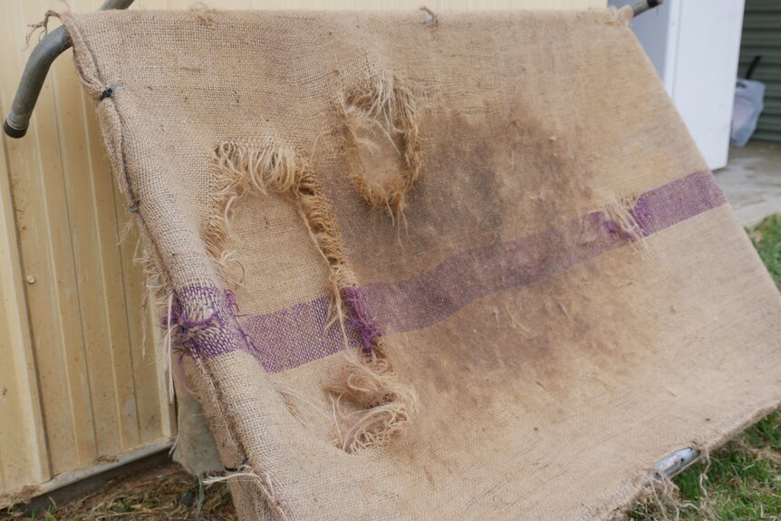A bed made out of a hessian material which is soiled and damaged.