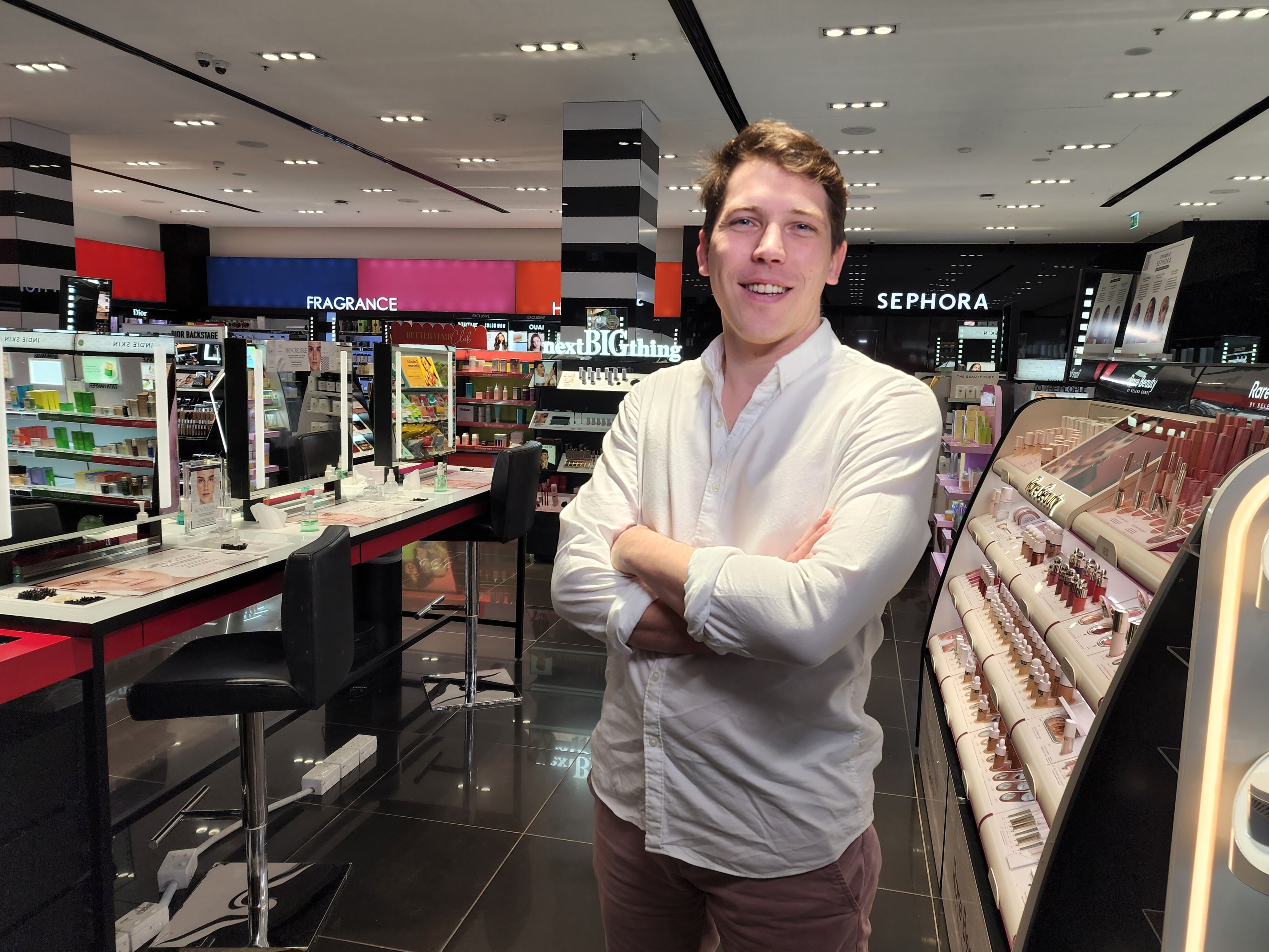A man with arms crossed in the cosmetic section of a shop