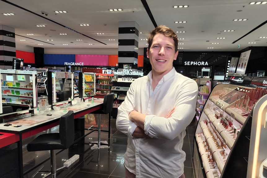 Un hombre con los brazos cruzados en la sección de cosmética de una tienda.