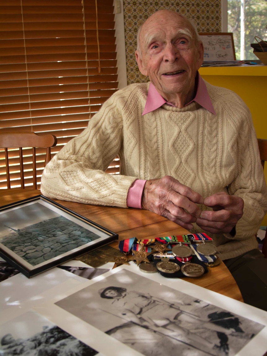 An old man sitting near war medals and photos smiles.