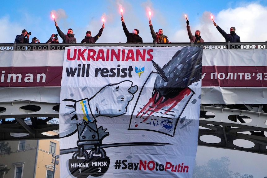 Ukrainians hold lights above a banner reading "Ukrainians will resisit" during a rally.