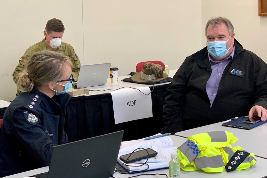 A CFA member sits with a police force member and an ADF soldier all working at desks