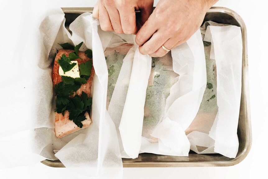 A tray of fish parcels, with butter, herbs and salt and pepper atop each piece of salmon from our easy recipe.