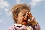 A girl wipes tears from her eyes as she cries in a dusty refugee camp.