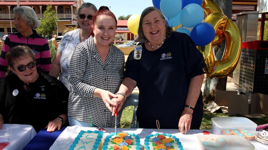 Two women are holding a knife and cutting into the CWA cake. 