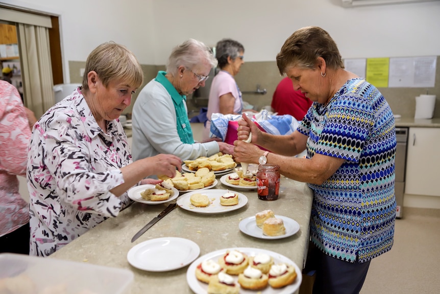 Older woman in kitchen piping jam and cream onto scones