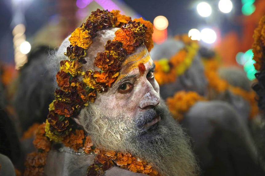 A close up of a holy man with a long beard dressed in orange flowers and pasted with ash.