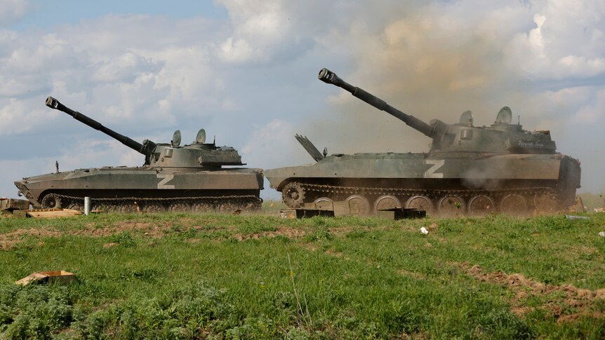 Two tanks in a green field fire towards Ukrainian army position.