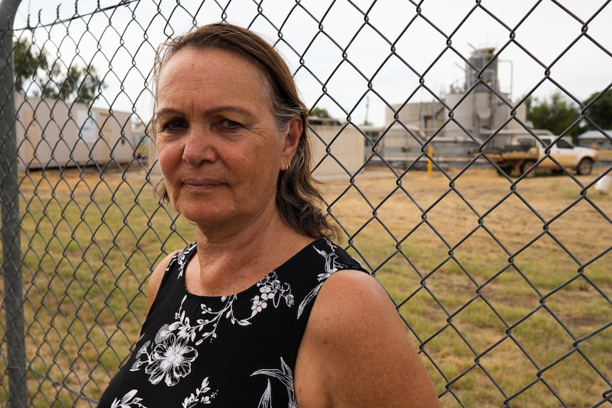 Woman wearing a black top with white florals standing in front of a fence.