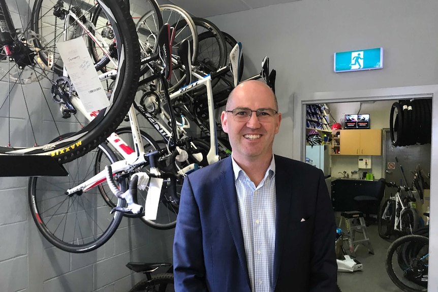 Peter Bourke stands in front of some bicycles in a shop.