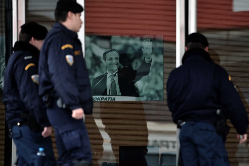 Riot police walk past a portrait of Greek prime minister Antonis Samaras.