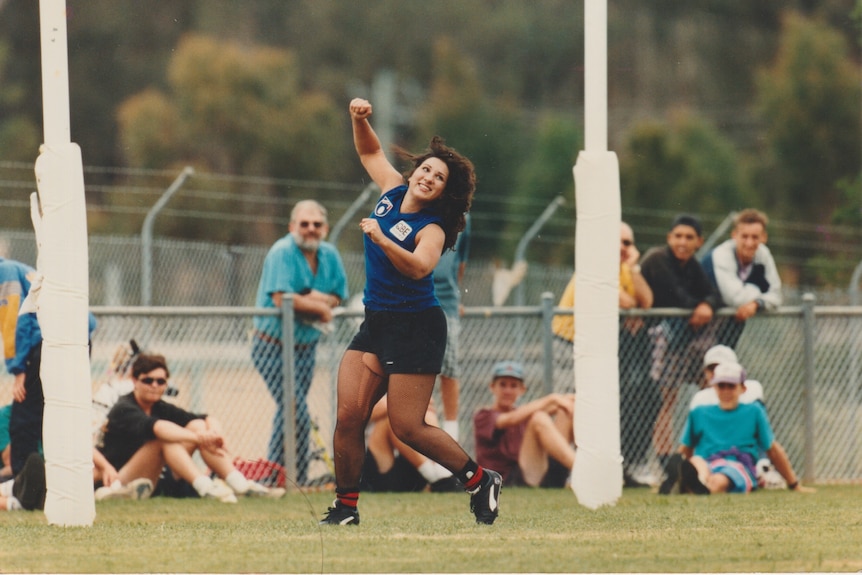 Old photo of Libbi running on a grass field in an AFL uniform and stockings.