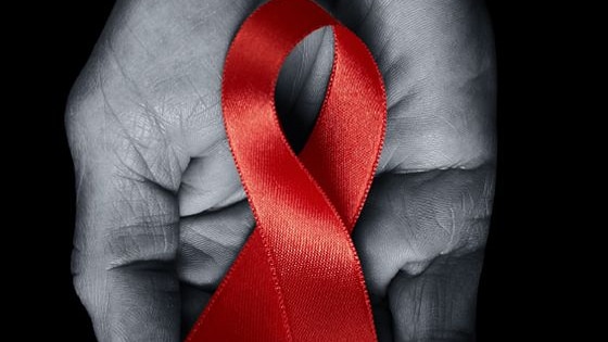 A black and white photograph of a person's hand holding a red HIV/AIDS awareness ribbon.