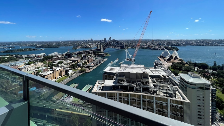 On a sunny day, you view the glittering waters of Sydney harbour several floors up. The Harbour bridge is in the foreground.