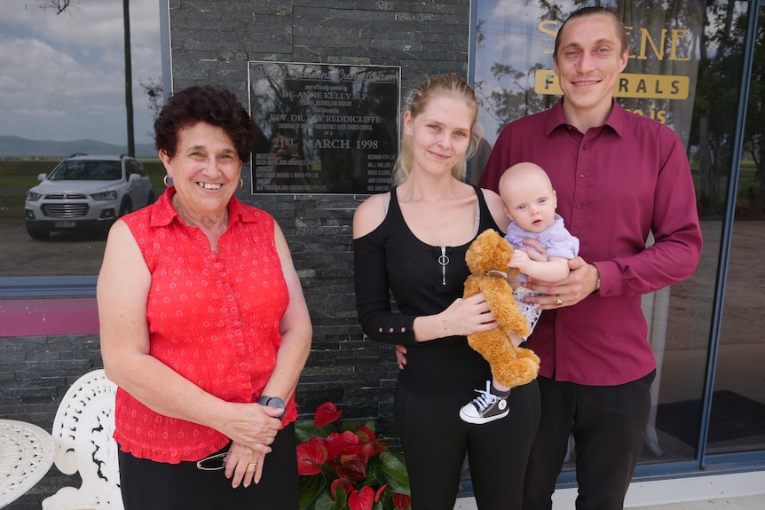 Two women and man and baby stand outside a funeral home. 