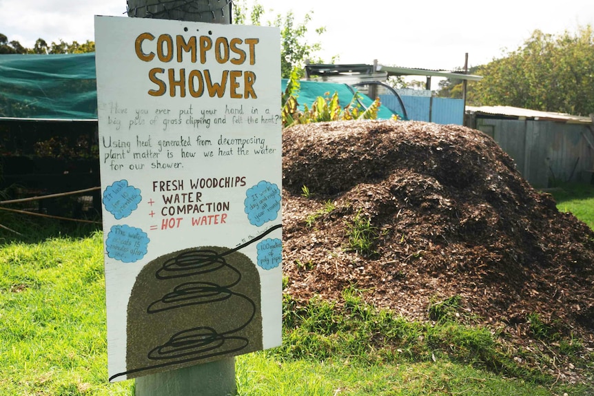A sign posted to a pole showing how the compost shower works. There is a pile of woodchips in the background