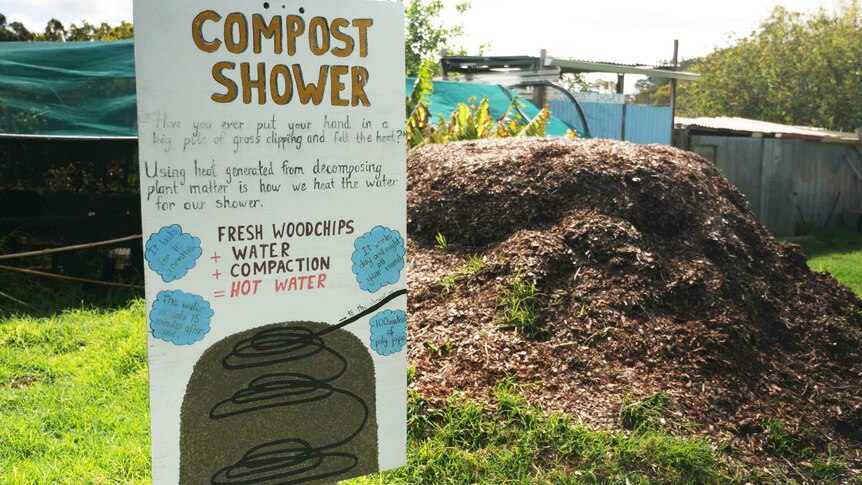 A sign posted to a pole showing how the compost shower works. There is a pile of woodchips in the background