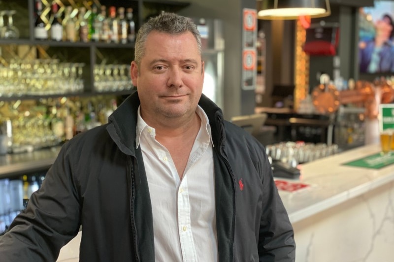 A man with short grey hair standing in a hotel bar.