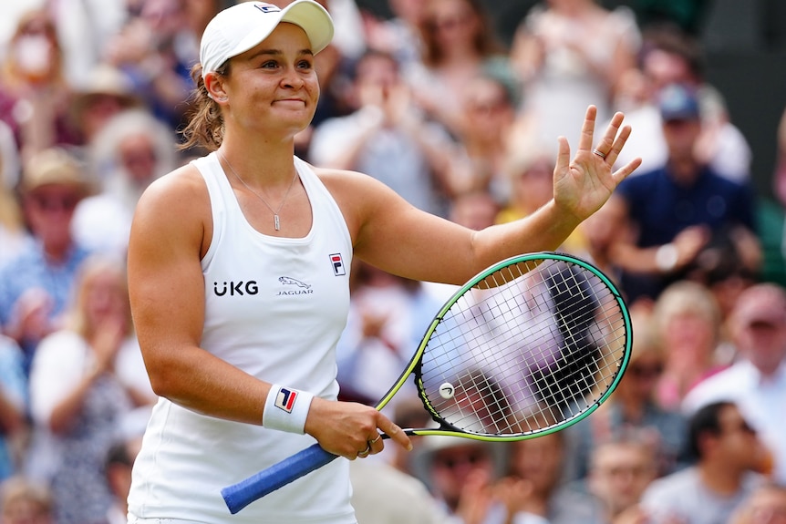 Ash Barty smiles and claps her racquet.