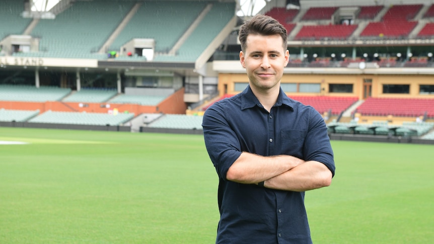 Aaron Bryans, standing in the middle of the Adelaide Oval, with an empty grandstand behind him.
