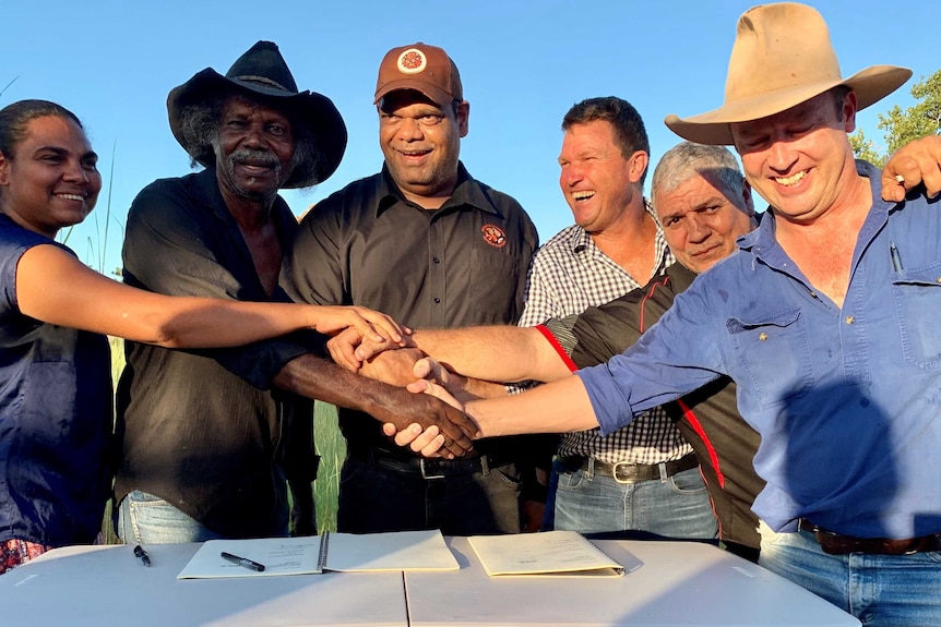 An Aboriginal woman, three Aboriginal men and two pastoralists shake hands