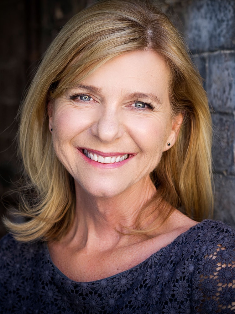 A headshot of Karen Cobban smiling at the camera in front of a blue brick wall.