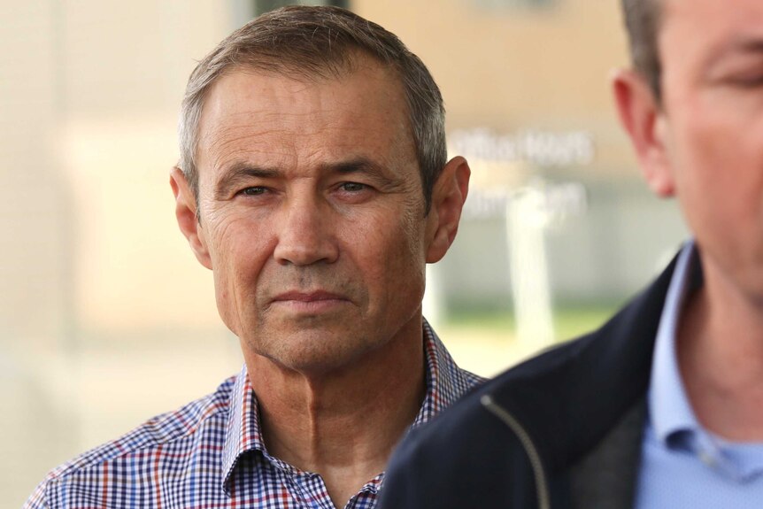 WA Health Minister Roger Cook looks contemplative as he stands listening to Mark McGowan speak.