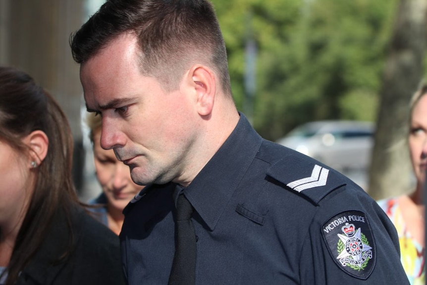 A photo of a man in a police uniform walking into court.