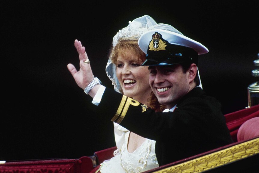 Prince Andrew waves as he sits in a carriage next to Sarah, Duchess of York. He wears black military garb and she wears a gown.