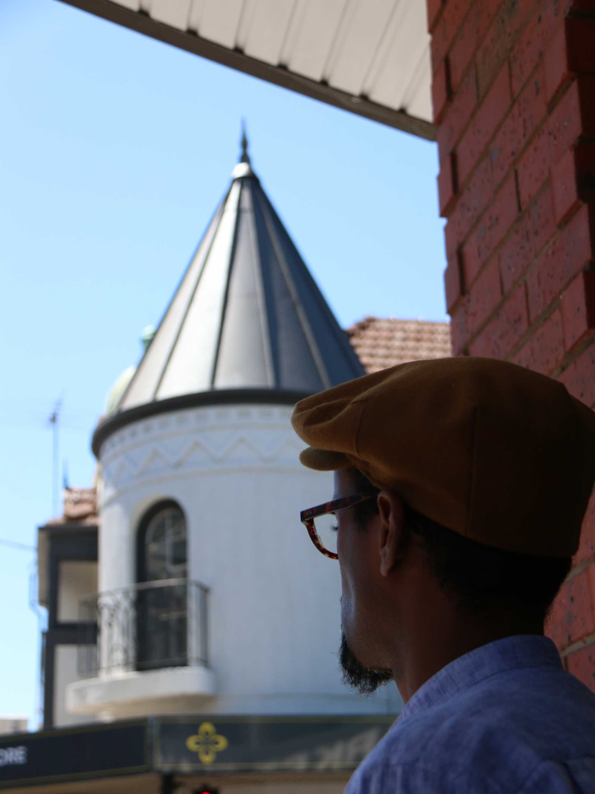 Nur Warsame in front of a building with a pointed roof.