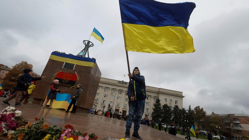 A boy waves a Ukrainian flag  while standing in a town square in front of a large municipal building. 