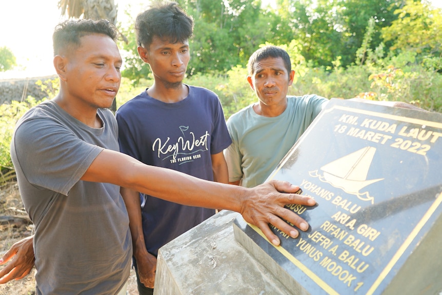 Three men look at a plaque commemorating people lost at sea in 2022.