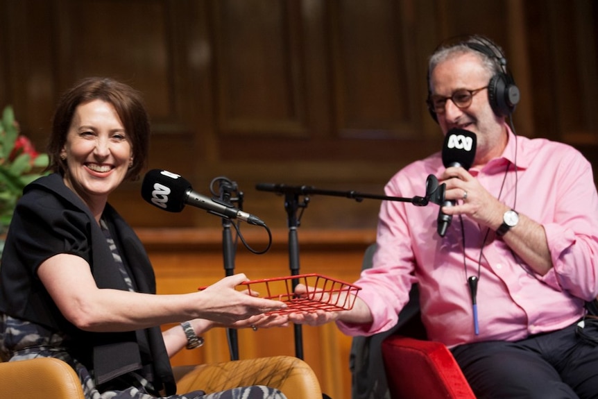 Virginia Trioli grins as Jon Faine hands her a document tray on stage.