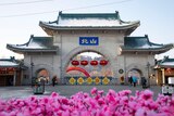 An arched gateway with Chinese writing and red lanterns on it, pink flowers out of focus in the foreground