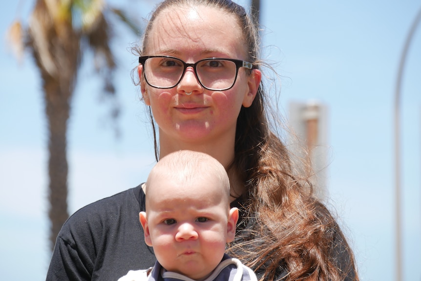 Woman wears glasses baby strapped to her chest in a carrier.