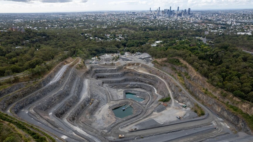 An image of a quarry with two pools of water in the middle surrounded by bushlands and the Brisbane skyline in the distance.