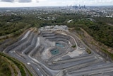 An image of a quarry with two pools of water in the middle surrounded by bushlands and the Brisbane skyline in the distance.
