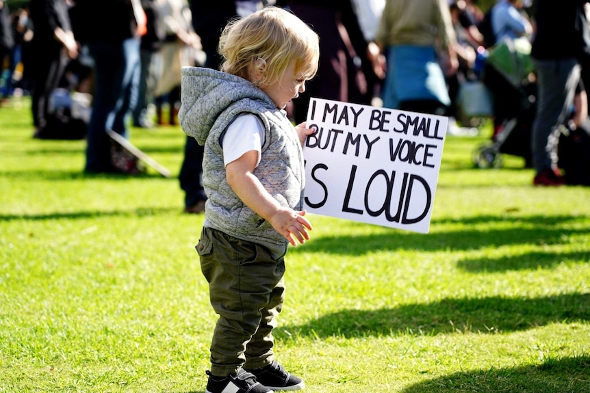 A toddler carries a sign saying 'I may be small but my voice is loud'.