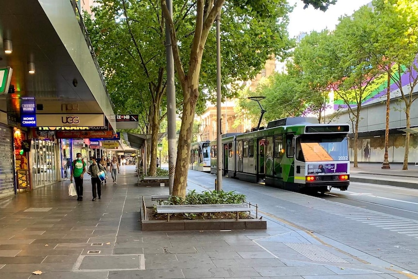 A small number of people walk down Swanston Street in Melbourne CBD as an empty tram goes past.