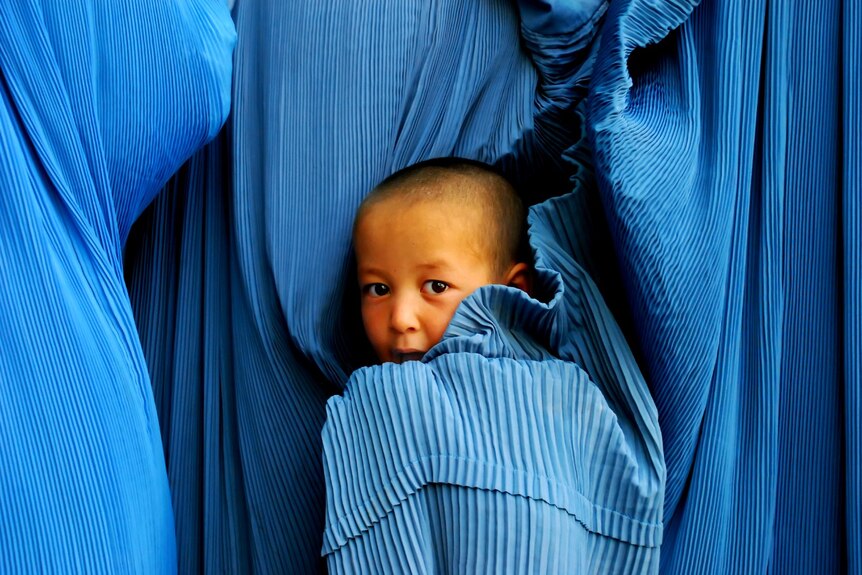 an Afghani child in the back of mum wearing burqa.
