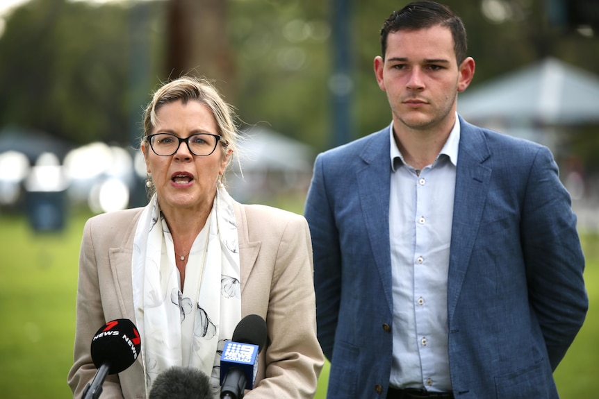 Libby Mettam wears a beige jacked and white shirt and stands alongside Peter Hudson who wears a blue blazer