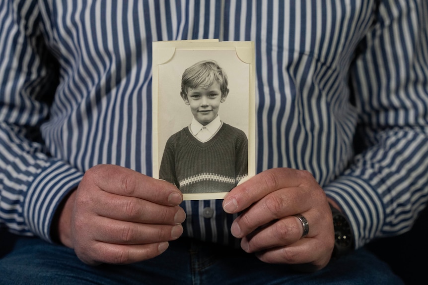A man's hands hold a black and white photo of a boy