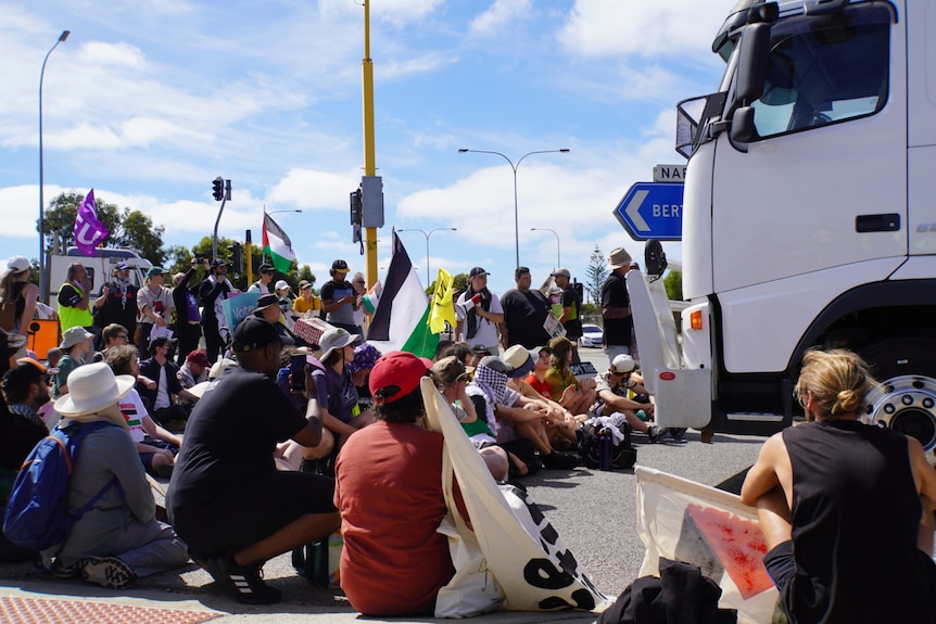 Dozens of protesters sitting in front of truck.