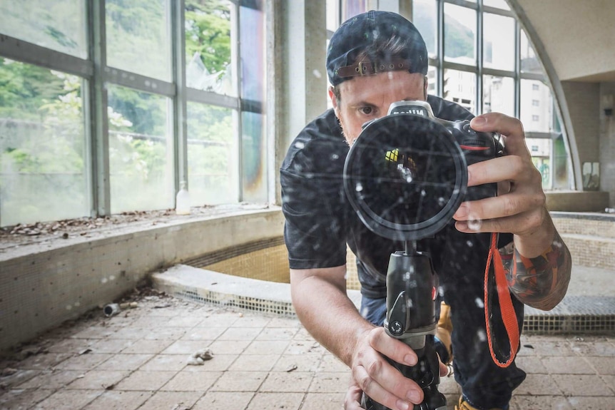 Brett Patman stands in a large room taking a photo of himself in front of a reflective service