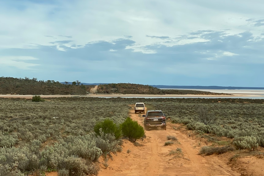 Two 4WD vehicles driving on sandy track towards a salt lake in the distance.