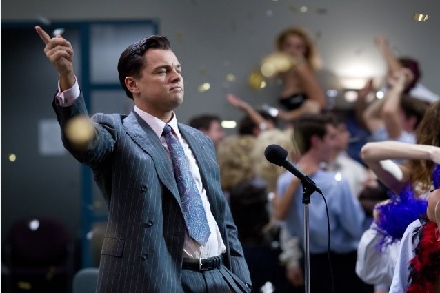 Actor Leonardo Dicaprio, a white man with brown hair, in suit leaning back and clicking his fingers in a scene.