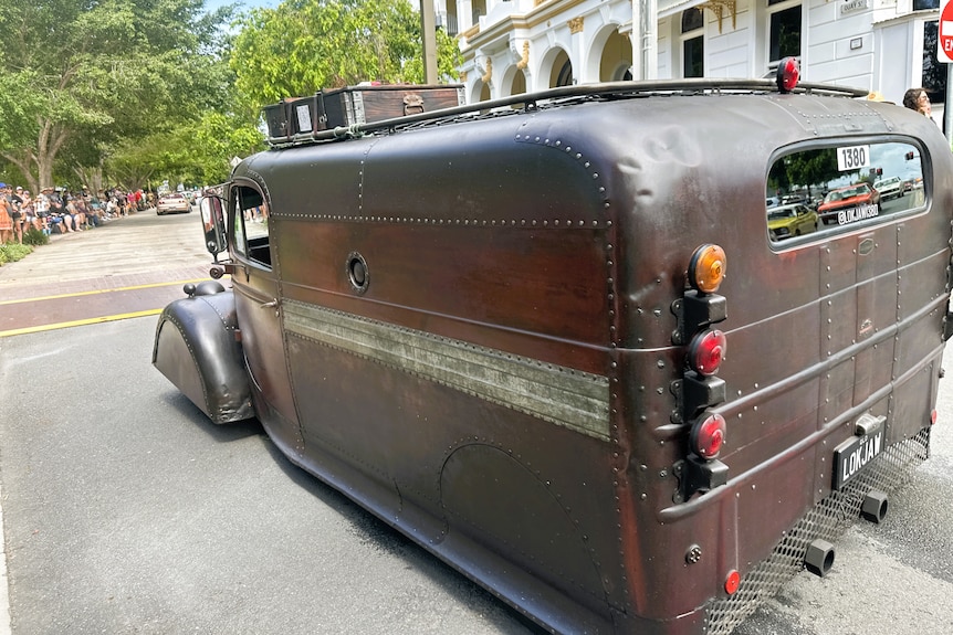A vintage hot rod which looks like an old medicine bag takes part in a street parade.