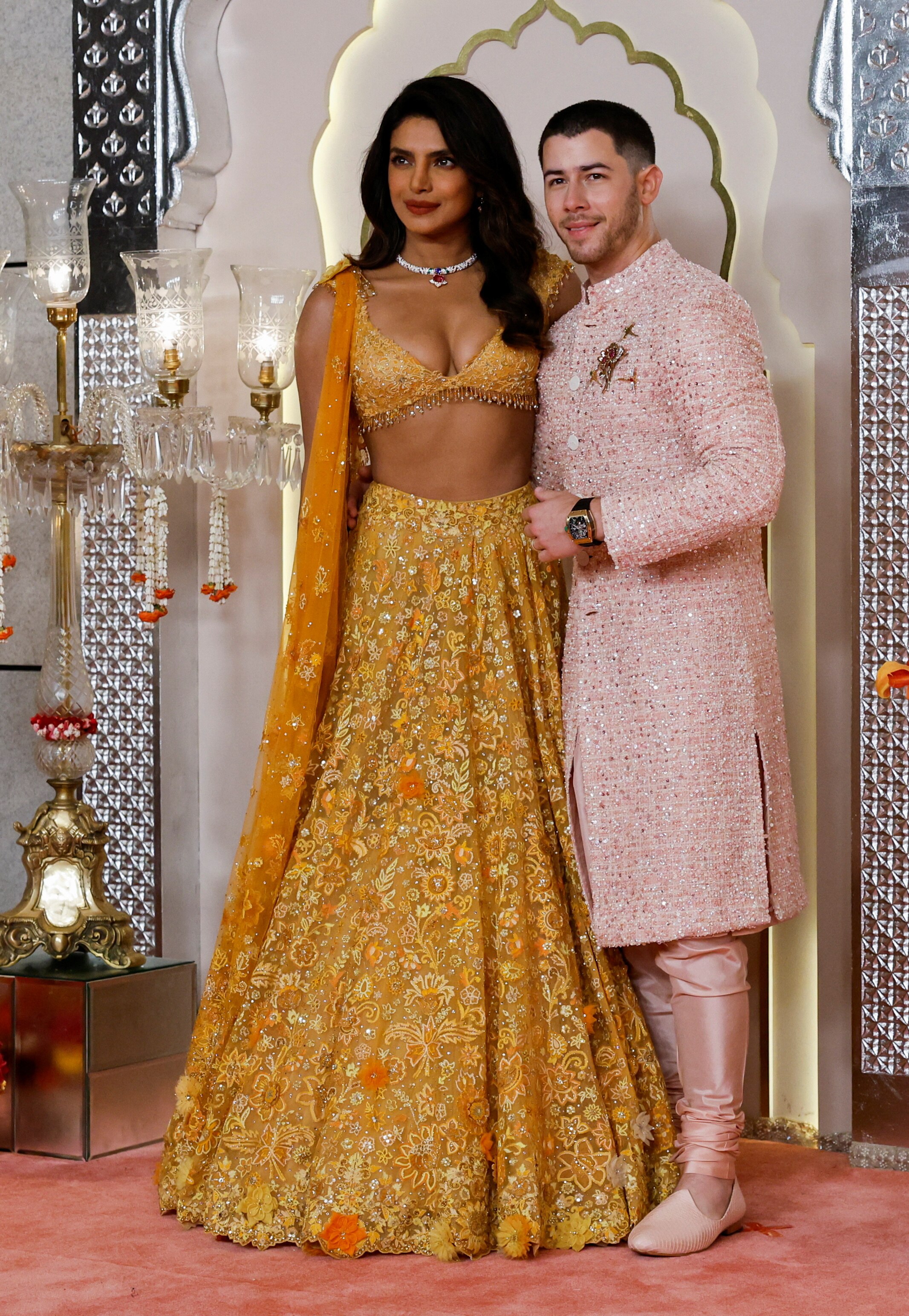 Priyanka Chopra wearing an embellished yellow skirt and matching crop top, while Nick Jonas wears pale pink