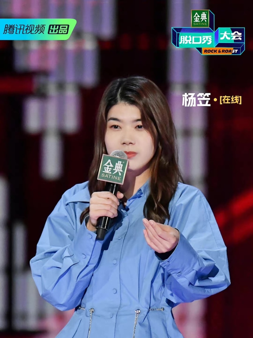 一位身穿蓝色衬衫的中国妇女对着麦克风讲话