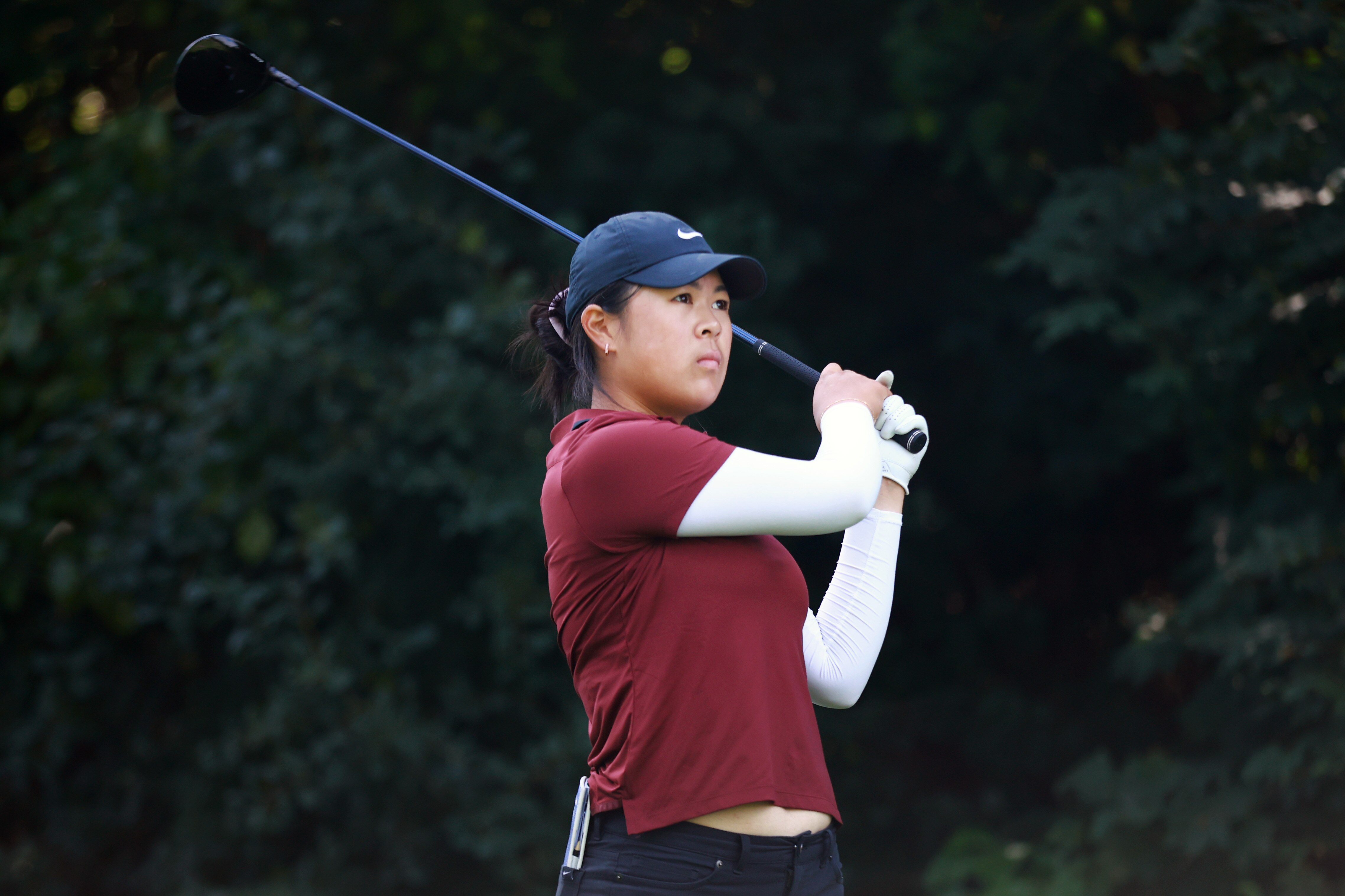 A young female golfer completes her tee shot as she looks down the fairway.